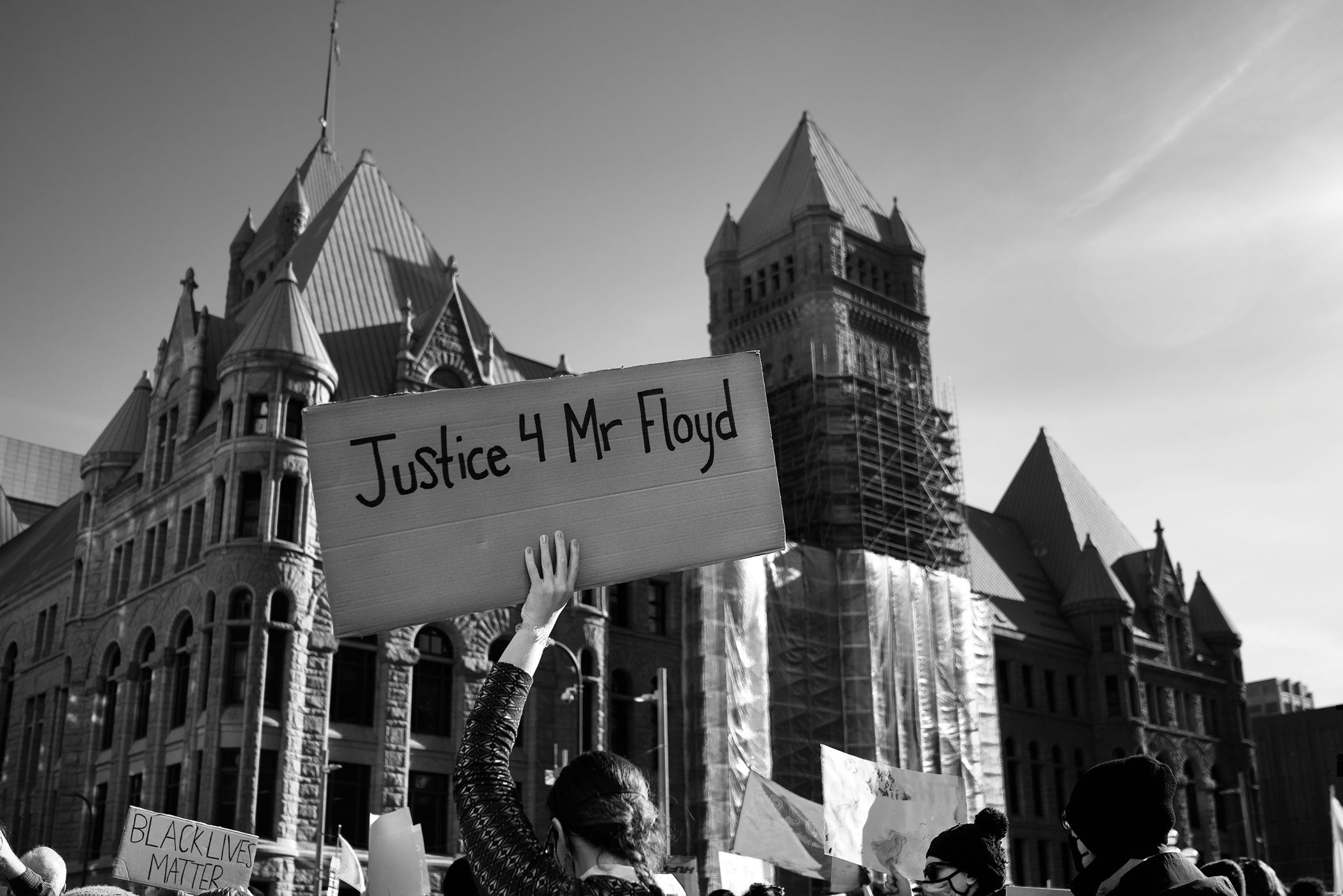 Amongst a crowd of people, a person holds a "Justice 4 Mr. Floyd" sign outside City Hall in downtown Minneapolis