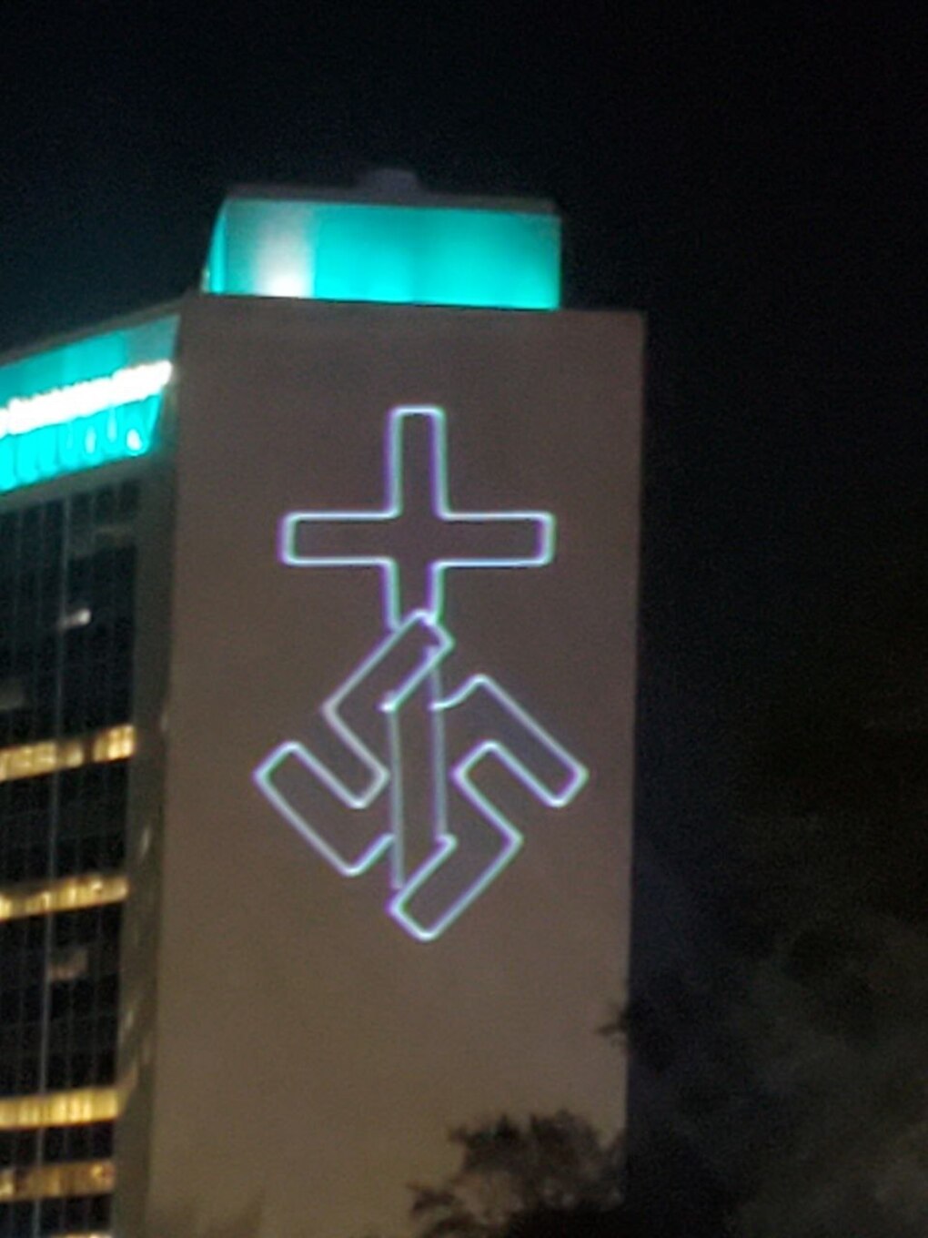 An image of a projection on a building that shows a Christian cross intertwined with a swastika.