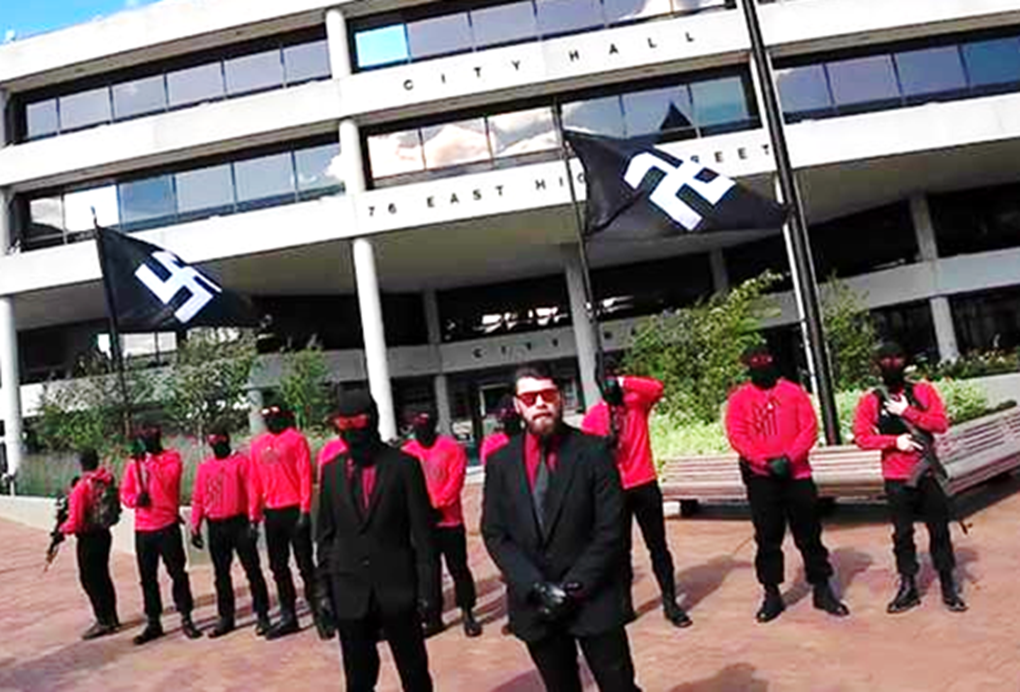 12 members of the white supremacist group Blood Tribe, wearing black masks and red shirts, hold swastika flags in front of city hall in Springfield, OH, August 2024.